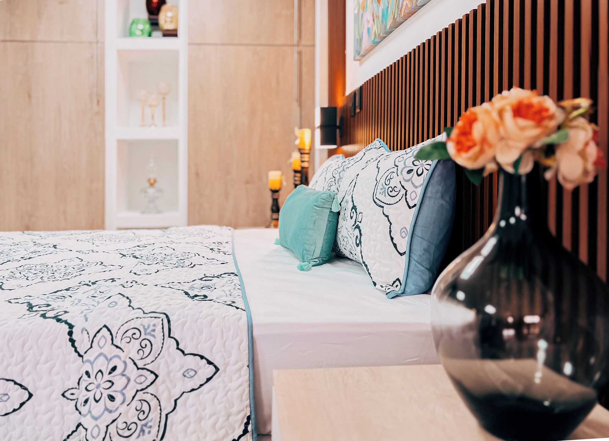 Ein aufgeräumtes Schlafzimmer mit Bett, Kissen, einer Blumenvase und einem Nachttisch.