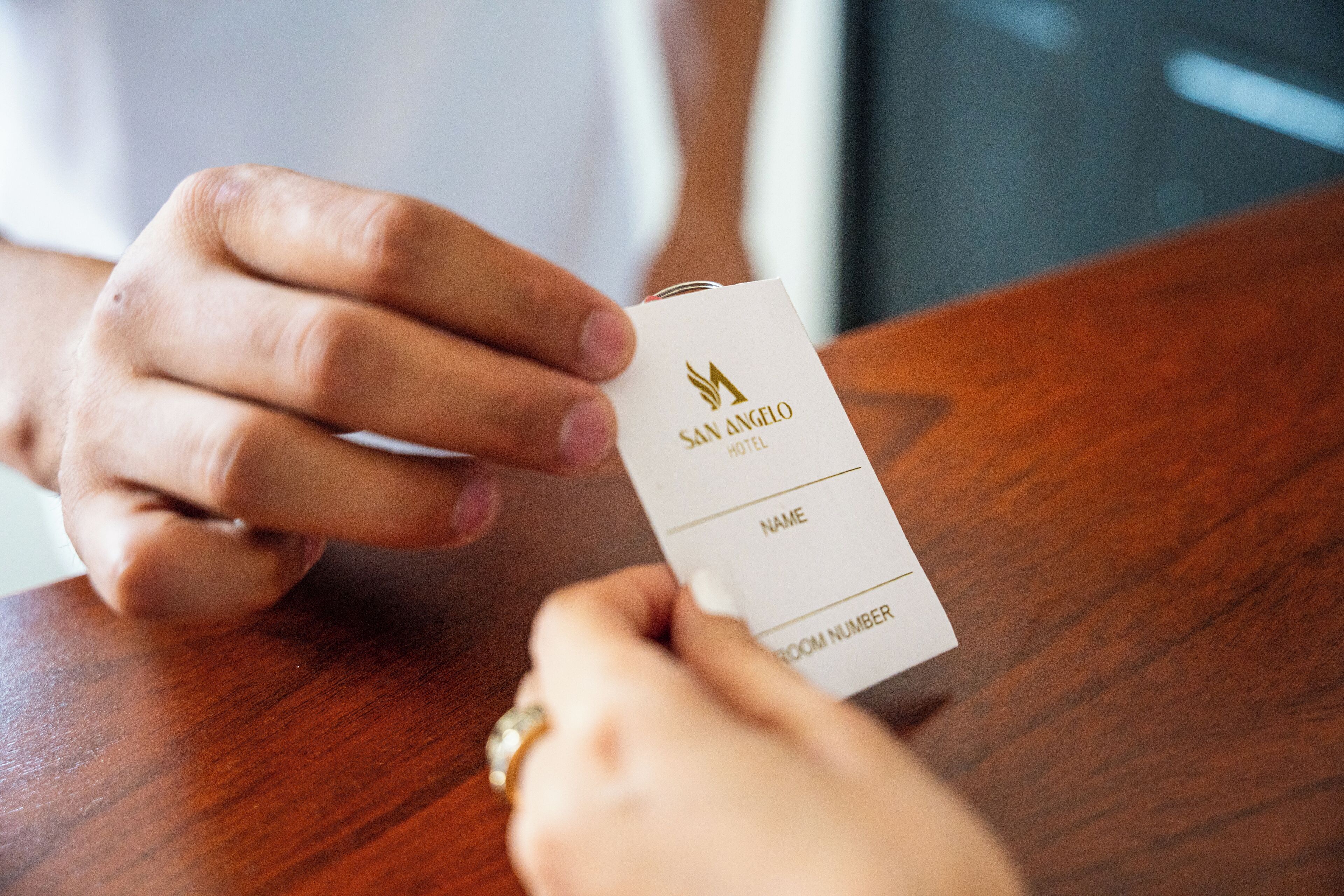 A person holding a hotel room keycard with the name "SAN ANGELO HOTEL" visible.