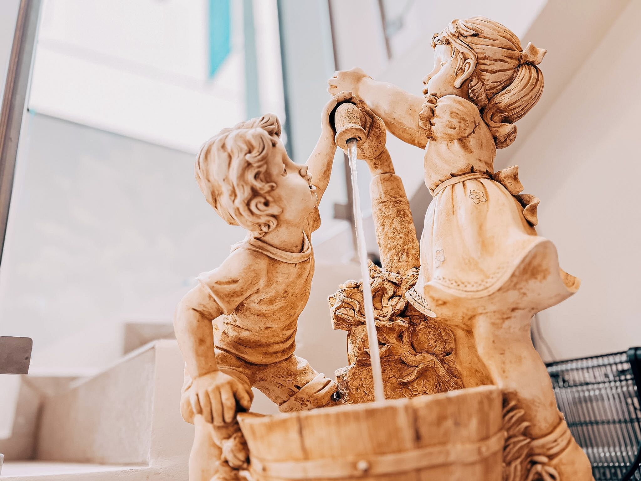 Une fontaine en marbre représentant deux personnages, un adulte et un enfant, dans un décor intérieur.