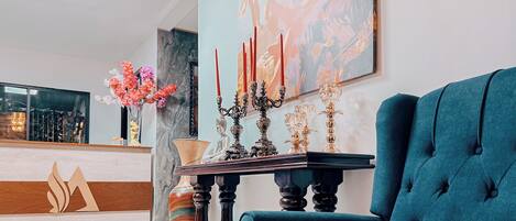 Un sillón tapizado en color aguamarina, un candelabro con velas rojas y un florero lleno de flores coloridas.
