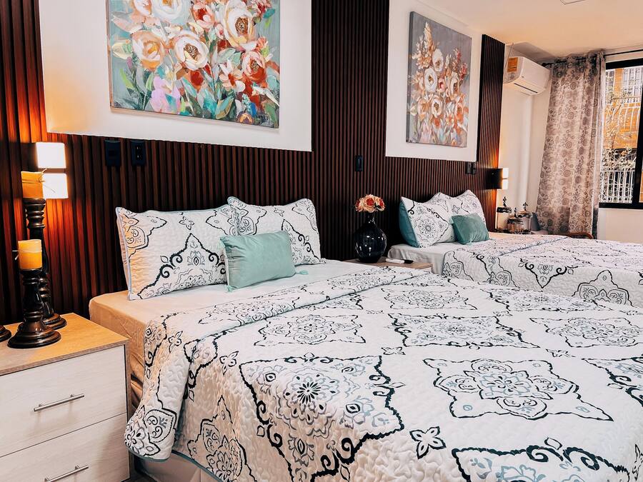 A bedroom with two beds, a nightstand, a dresser, and wall art.