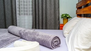 A neatly made bed with a rolled-up purple blanket, a white pillow, and a white towel on a purple bedspread. - Bustani Luxury Homestay (Moshi)