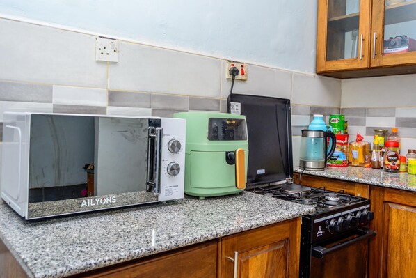 A kitchen with a microwave, toaster, coffee maker, and stove. - Bustani Luxury Homestay (Moshi)