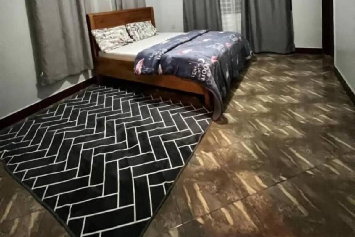 Une chambre à coucher avec un lit, des rideaux gris, un tapis à motifs et un plancher en bois.