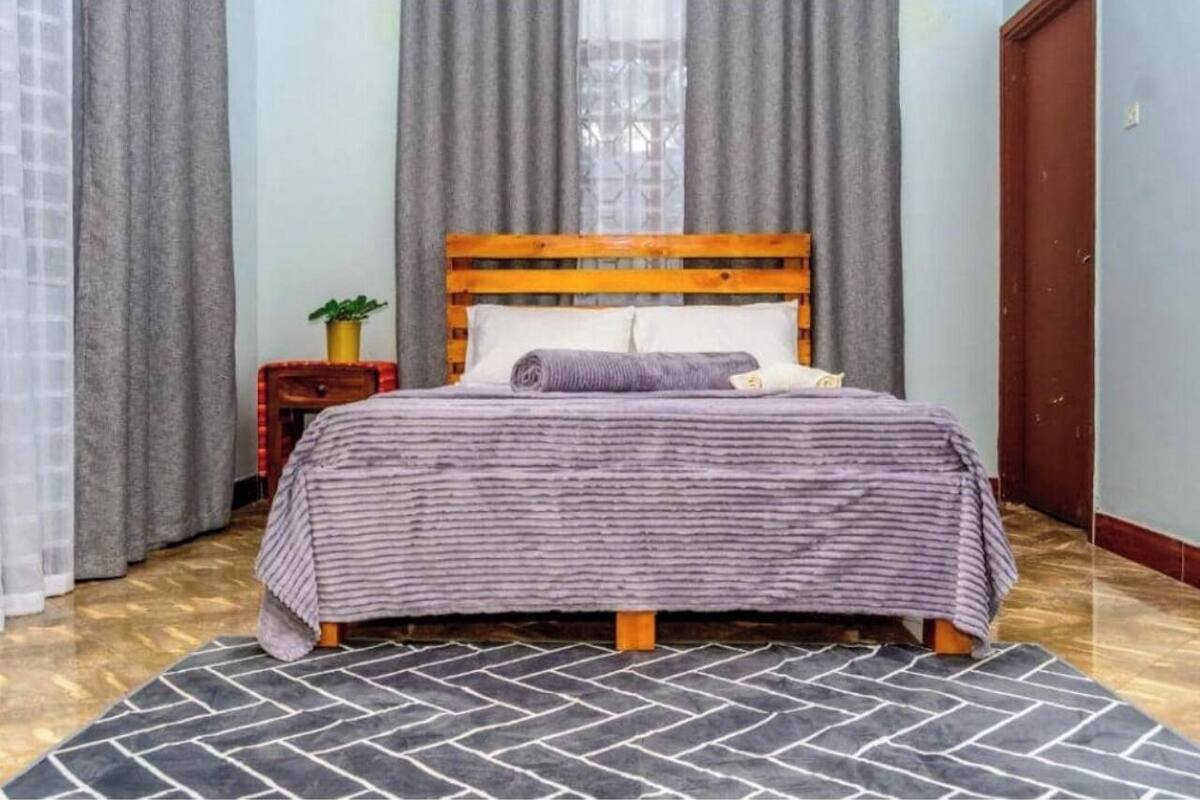 Une chambre à coucher avec une tête de lit en bois, un lit recouvert d’une couvre-lit à rayures, une table de chevet ornée d’une plante et un tapis à motifs.