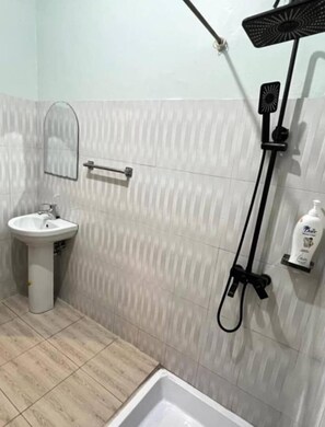 A bathroom with a sink, mirror, shower, and a bottle of hand soap. - Bustani Luxury Homestay (Moshi)