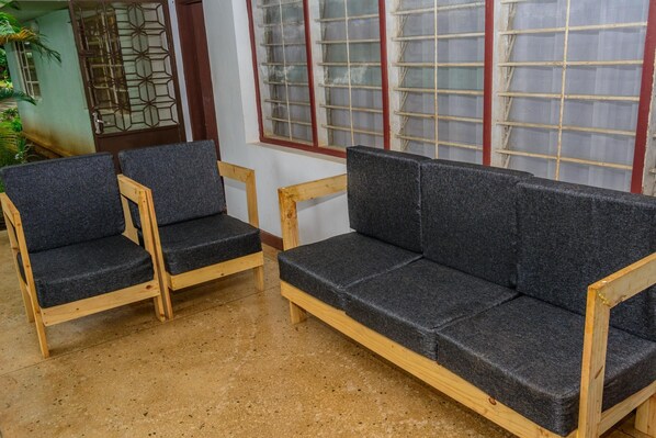 A room with a wooden sofa and two matching armchairs, a window with a metal grid, and a door with a decorative metal grille. - Bustani Luxury Homestay (Moshi)