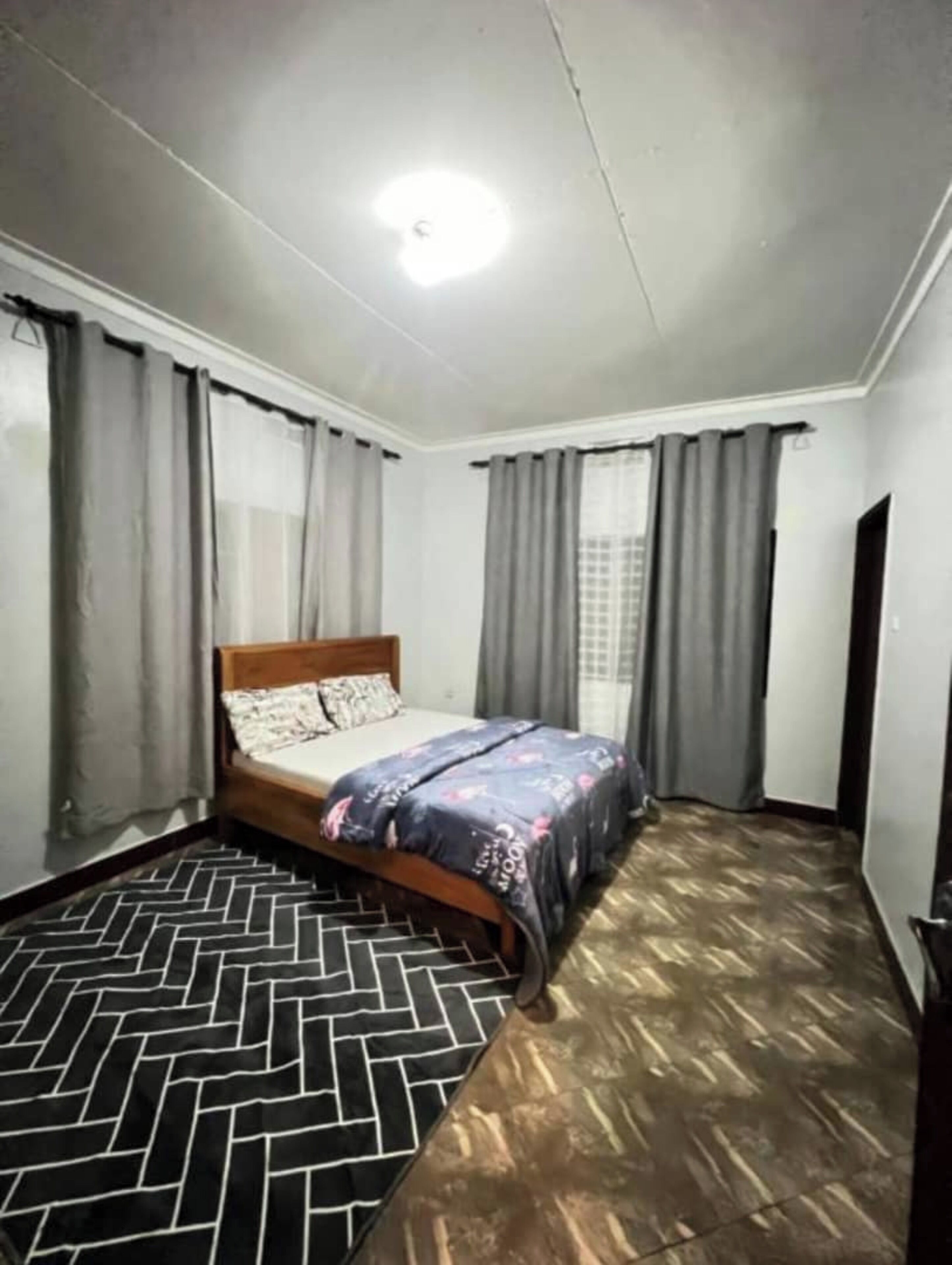 A bedroom with a bed, curtains, a patterned rug, and a wooden floor.