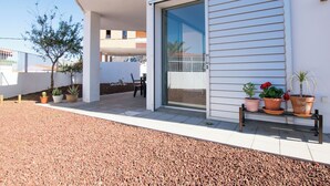 Un bâtiment moderne doté d’une porte coulissante en verre, d’un espace extérieur aménagé pour s’asseoir et de plantes en pot.