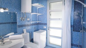 Une salle de bain équipée d’un lavabo, de toilettes et d’une douche, avec des carreaux de mosaïque bleus et des accessoires blancs.