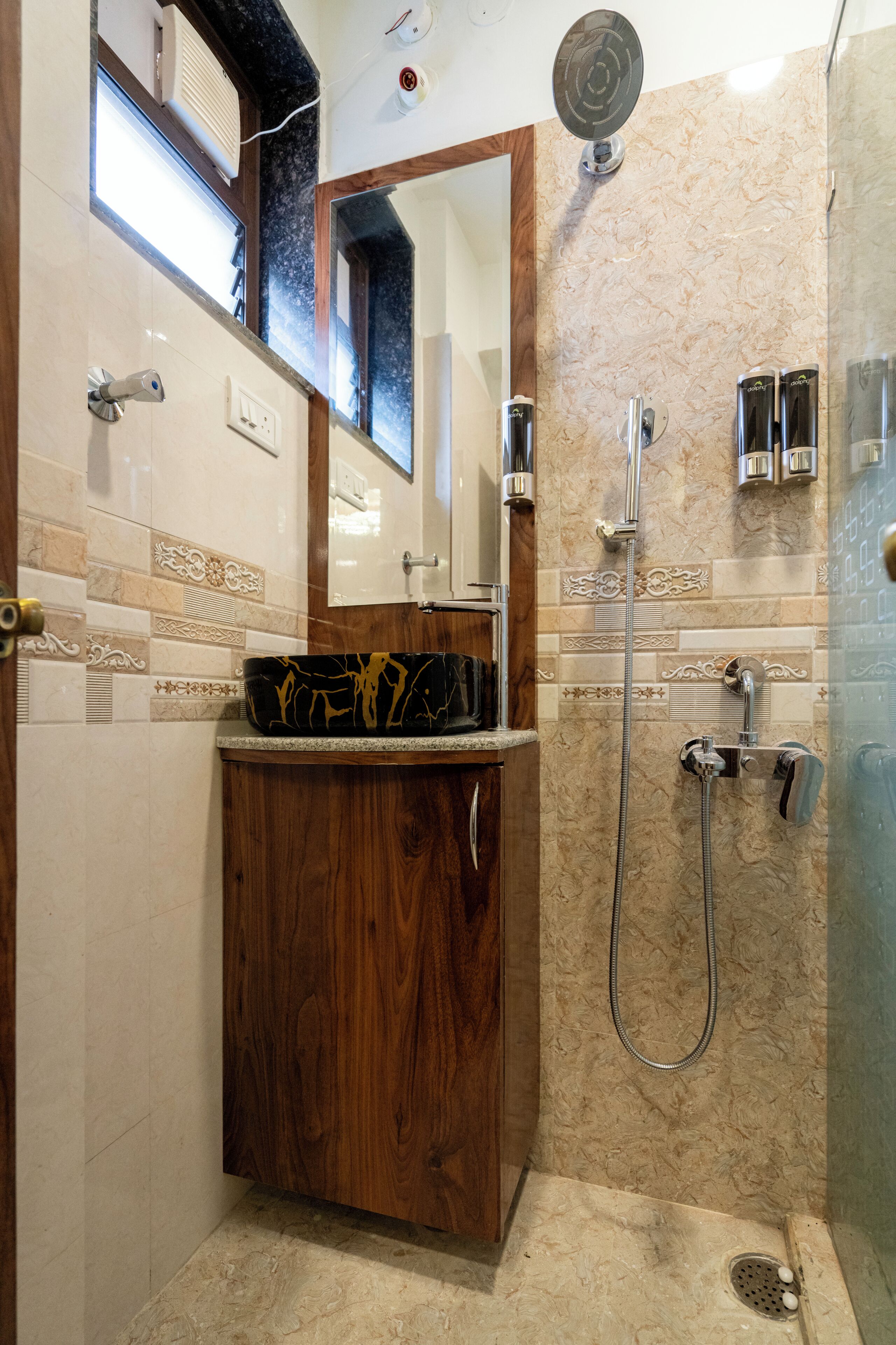 Un baño con tocador de madera, un espejo, ducha con cabezal de ducha manual y cabina de ducha con mampara de vidrio.