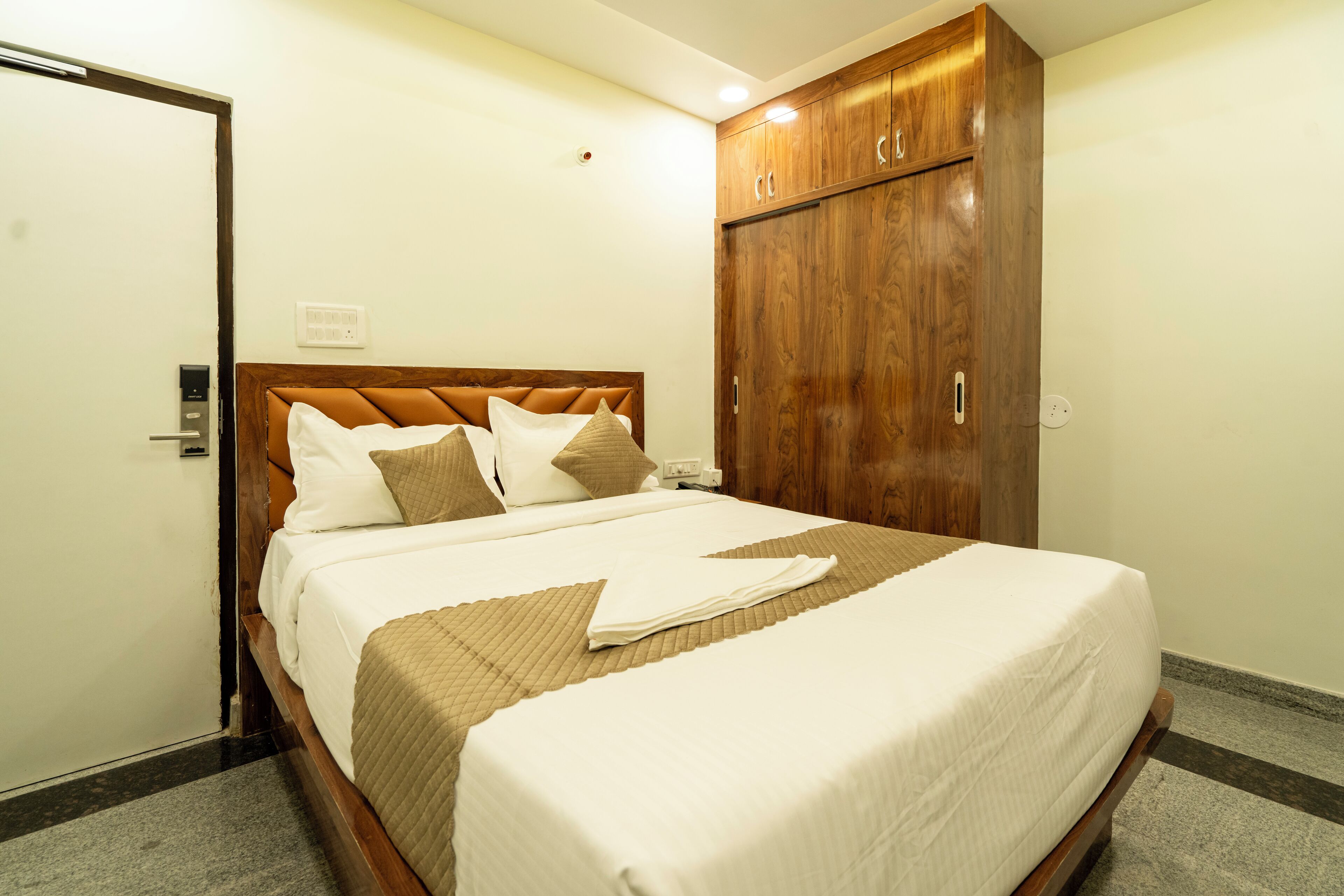 A neatly made bed with a wooden headboard, a large wardrobe, and a door to the left.