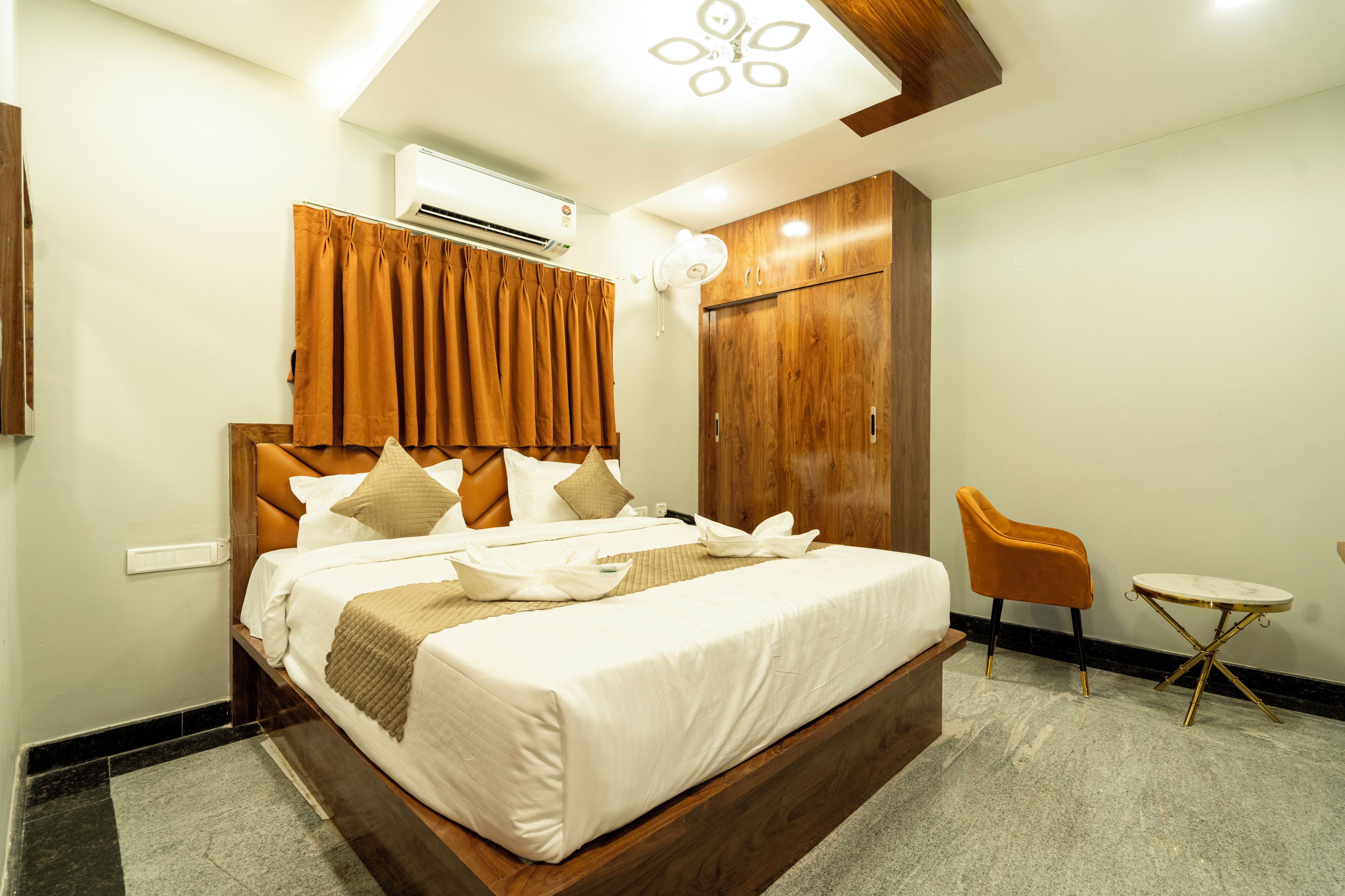 A hotel room with a large bed, wooden headboard, a small round table, a chair, and a wardrobe.