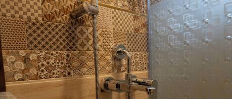 Une douche équipée d’un pommeau de douche à main et d’un robinet mural. L’espace douche est agrémenté de carreaux décoratifs sur les murs et d’une porte en verre.