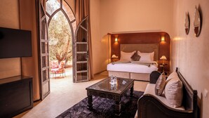 A hotel room with a large bed, a TV, a coffee table, and a view through an arched window. - Palais Menzah & SPA (Oulad Hassoune)