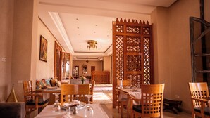 A dining area with wooden furniture, a chandelier, and a decorative partition. - Palais Menzah & SPA (Oulad Hassoune)
