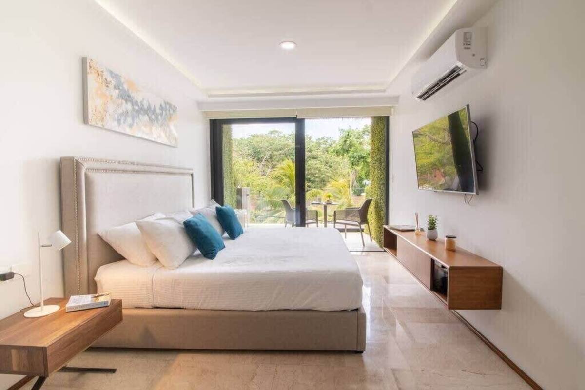 A modern bedroom with a large bed, a TV mounted on the wall, and a view of the outdoors.