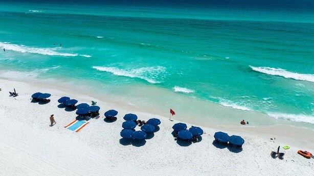 Une plage aux eaux turquoise et limpides, au sable blanc et aux parasols bleus.