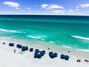 Een strand met helder turquoise water, wit zand en blauwe parasols.