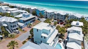 Un quartier résidentiel situé sur la côte, avec de nombreuses maisons à deux étages, une piscine et une plage en arrière-plan.