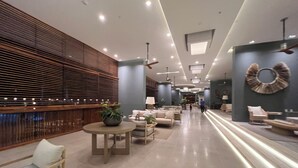 En rummelig lobby med moderne design, med et siddeområde med sofaer og et rundt bord, en træribbeklasket væg og et dekorativt vægkunstværk.