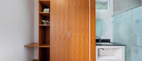 A wooden wardrobe with shelves, a bathroom with a sink and mirror, and a shower with floral tiles.