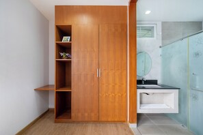 A wooden wardrobe with shelves, a bathroom with a sink and mirror, and a shower with floral tiles.