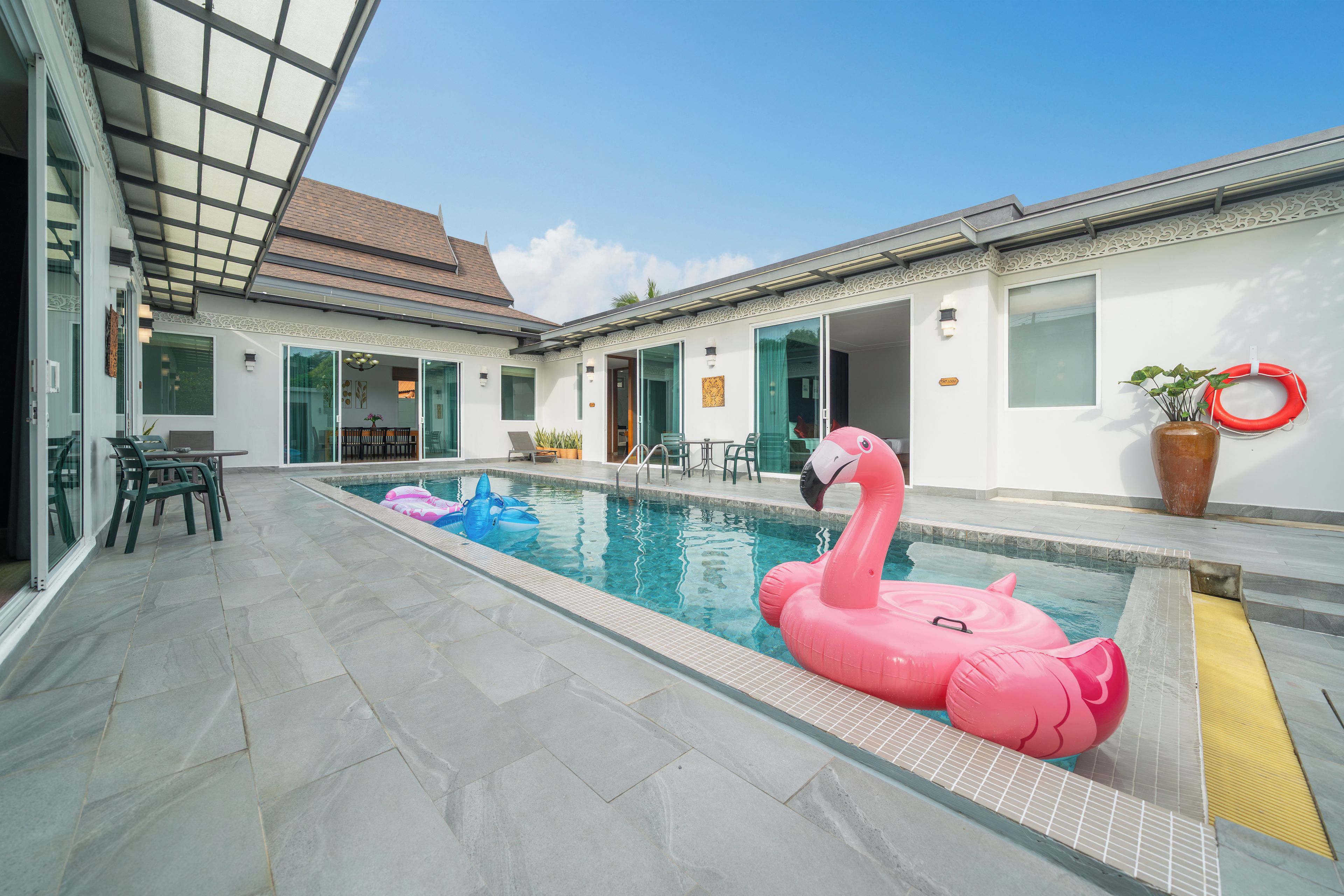 Une piscine avec un flotteur en forme de flamant rose, un autre flotteur gonflable bleu et un bouée rouge.