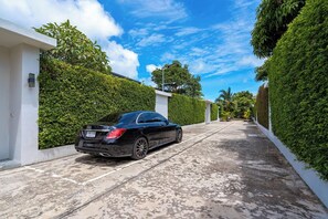 A black car parked on a paved driveway with a white wall and green hedge on one side and a white wall and green hedge on the other.