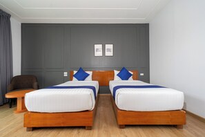 A hotel room with two wooden beds, a small wooden table, a brown armchair, and a grey wall with two framed pictures. - Phuket La Siesta Pool Villa And Pool Access (Rawai)