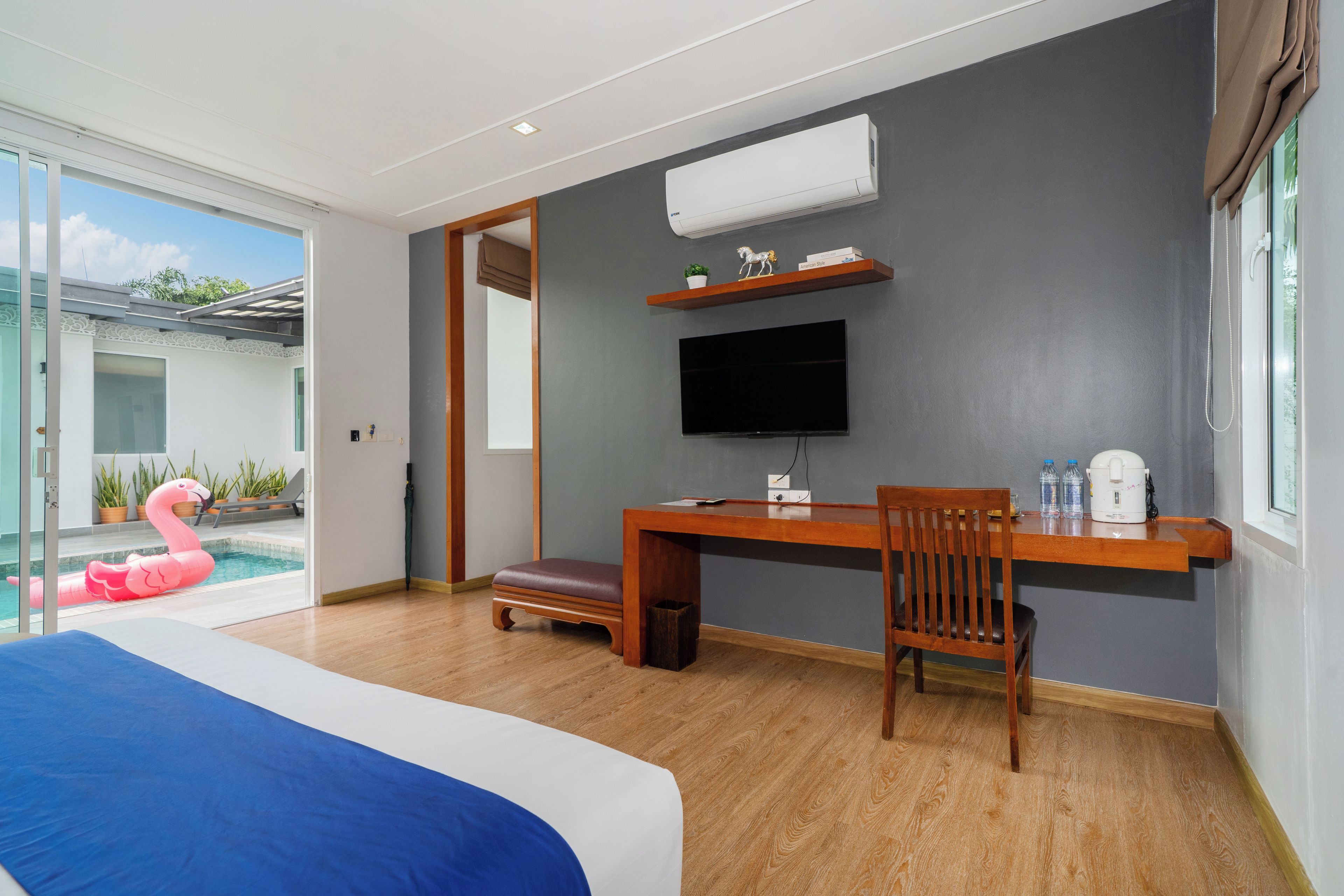 A modern hotel room with a large bed, a desk with a chair, a flat-screen TV, and a view of a swimming pool with a pink flamingo float.