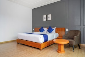 A neatly arranged bedroom with a wooden bed, a grey upholstered armchair, and a small wooden table. - Phuket La Siesta Pool Villa And Pool Access (Rawai)