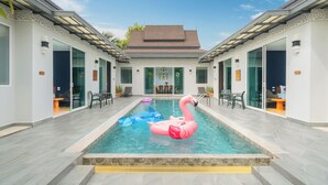 A swimming pool with decorative flamingos and a dolphin float, surrounded by a modern building with glass doors and a tiled floor. - Phuket La Siesta Pool Villa And Pool Access (Rawai)