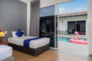 A hotel room with a bed, a nightstand, a lamp, a sliding glass door to a pool area with a pink flamingo float. - Phuket La Siesta Pool Villa And Pool Access (Rawai)
