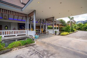 Fachada de hotel con porche cubierto, columnas y fuente de agua.