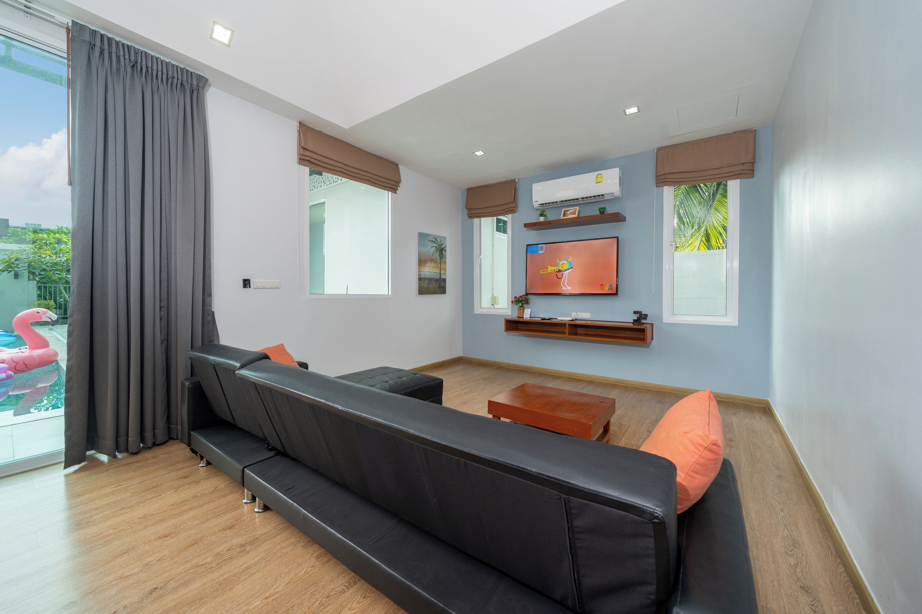 A modern living room with a black sofa, a wooden coffee table, and a flat-screen TV mounted on the wall.