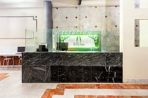 A hotel reception area with a marble counter, a chandelier, and a reception desk. - Capital O Nueva York, Guadalajara centro (downtown) (Guadalajara)