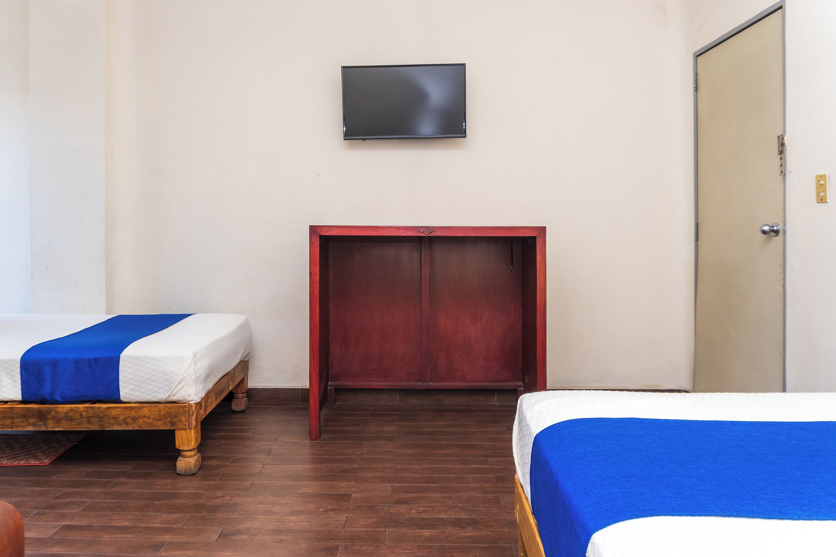 A room with two single beds, a TV mounted on the wall, and a wardrobe.