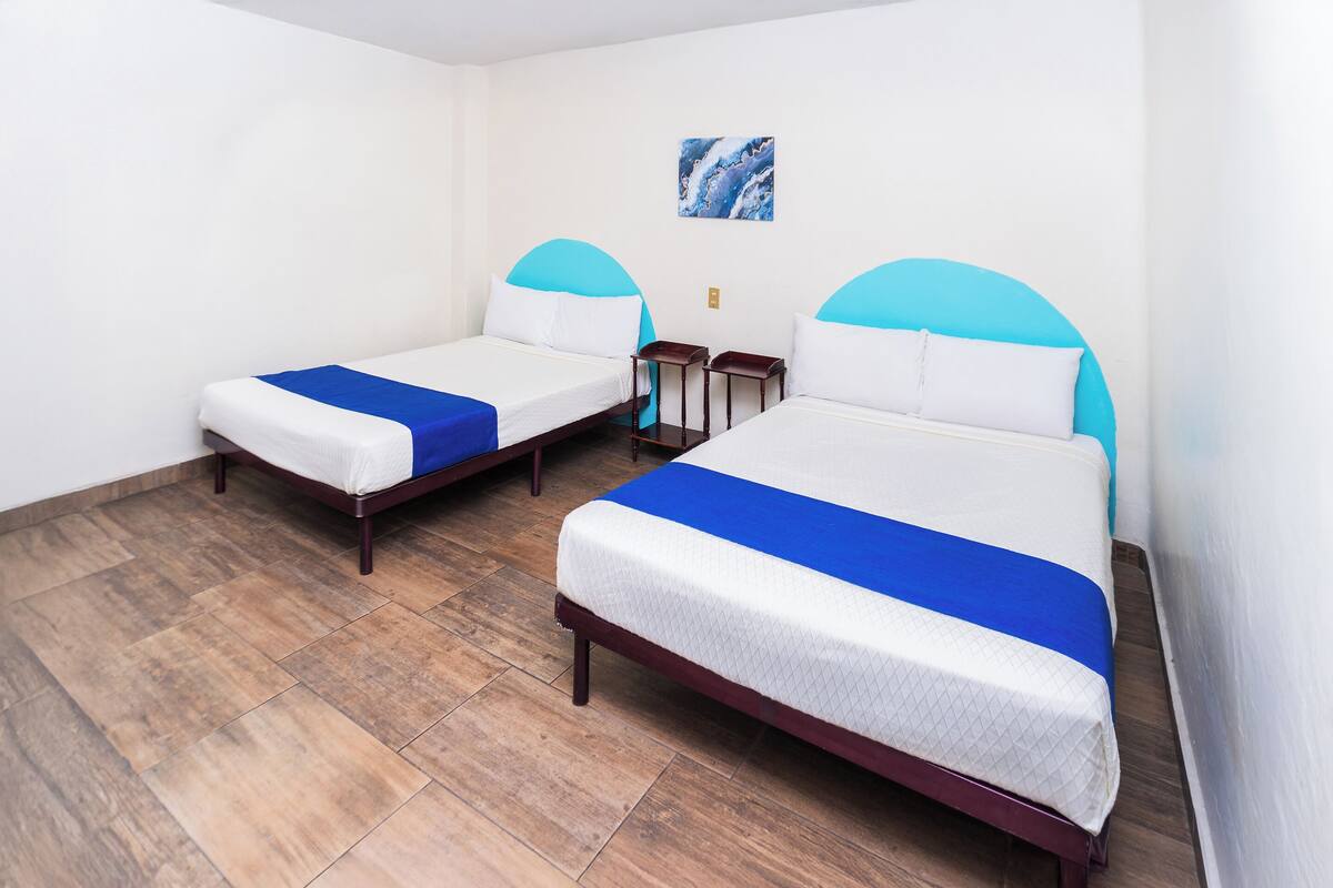 Une chambre d’hôtel avec deux lits, chacun doté d’une tête de lit bleue, de draps blancs et d’une petite table de chevet.