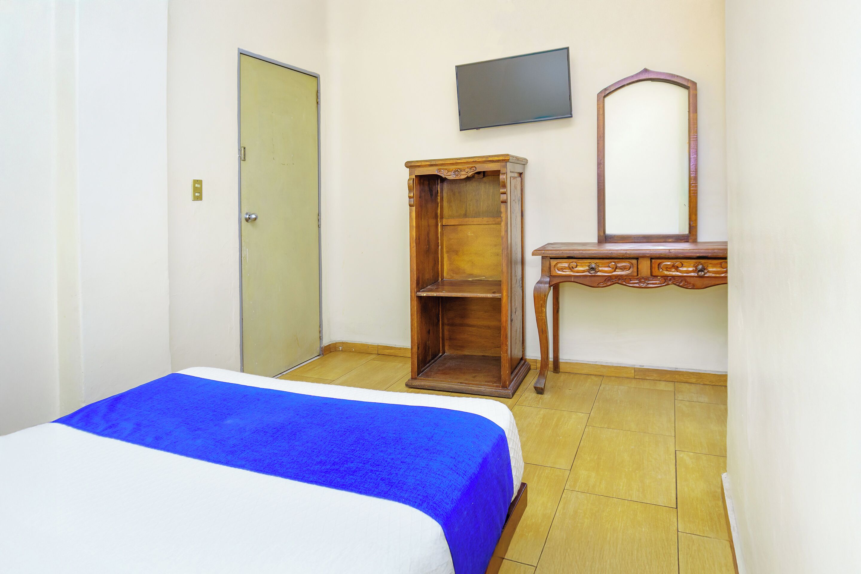 Een slaapkamer met een bed, een houten dressoir, een spiegel en een televisie aan de muur.