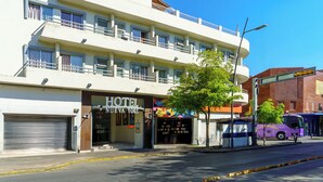 Ein mehrstöckiges Hotel mit einem Balkon im oberen Geschoss, einer geschlossenen Garagentür und einem violetten Bus, der auf der Straße geparkt ist.
