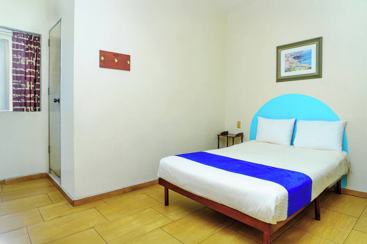 Une chambre à coucher avec un lit, une porte, un tableau accroché au mur et une petite table.