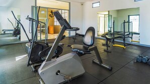 Ein Fitnessraum mit Trainingsgeräten, einem Spiegel und einer Tür zu einem weiteren Raum.