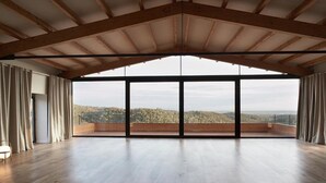 A spacious room with a high ceiling and large windows offering a view of a forested landscape. - Country house in Vilamaniscle - Girona (Vilamaniscle)
