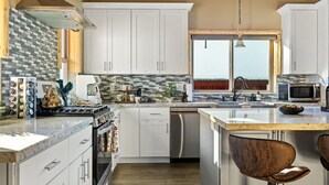 A modern kitchen with white cabinets, a large island, and a view through the window.