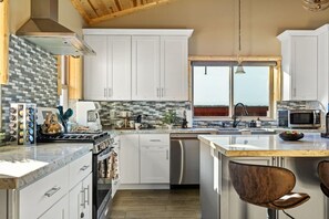A modern kitchen with white cabinets, a large island, and a view through the window. - High Altitude Retreat + Game Room + Hot Tub (Big Bear Lake)
