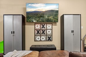 Una habitación con dos armarios grises, un cuadro grande enmarcados de un paisaje boscoso, y un tablero de juego fijado a la pared.