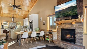 A spacious living room with a stone fireplace, a large TV mounted above it, and a cozy seating area with a cowhide rug.