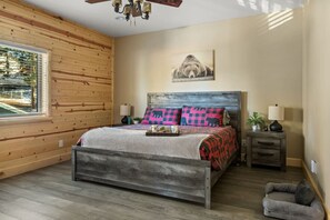 A bedroom with a wooden ceiling, a bed with a patterned bedspread, a nightstand with a lamp, and a wall-mounted picture.