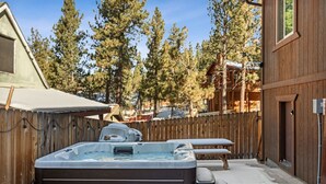 A hot tub in a backyard with a wooden fence, a wooden deck, and a building in the background.